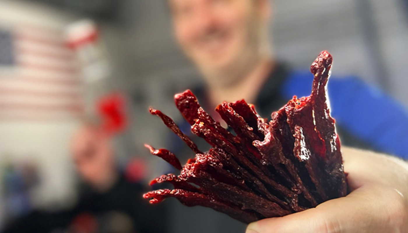 Homemade beef jerky sticks glisten with savory perfection my hand, showcasing their smoky, peppery flavor.
